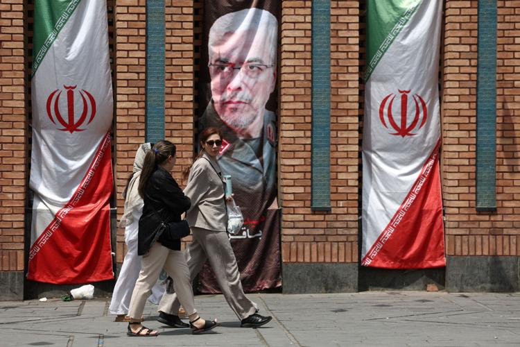 Iranian women walk past a banner with a picture of the former Chief of Staff of the Iranian Armed Forces, Mohammad Bagheri, in Tehran