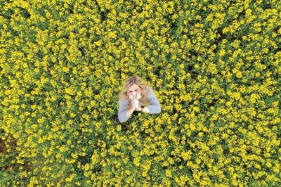Young woman suffers from allergy in a rape field and has to sneeze