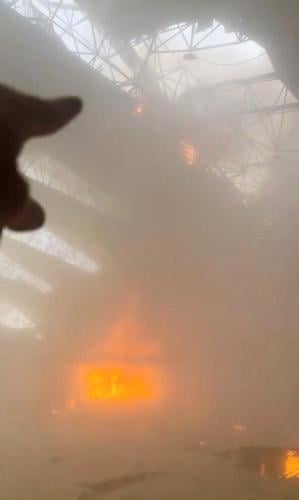 A person points to the damage on the roof as flames and smoke rise from a fire in the aftermath of Iranian strikes at Kuwait International Airport in Kuwait City