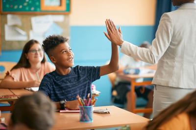 Elementary student and his teacher giving high five during class at school.