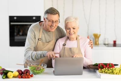 Couple Cooking And Using Laptop