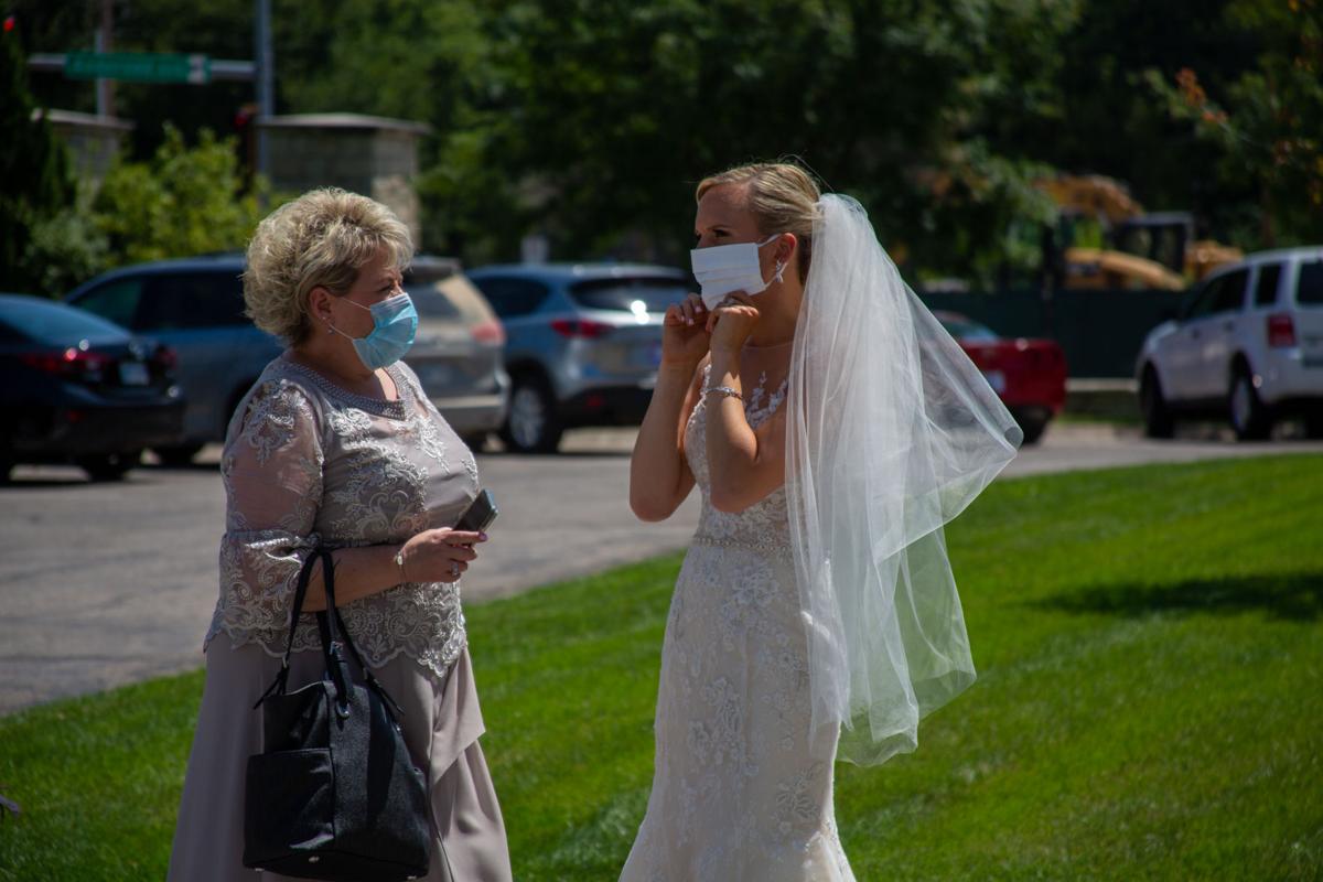 Bride Brittany Murrell puts on mask to match dress at wedding. Brittany Murrell and Matthew Lorson held reception at the Alumni center hosting a “drive by wedding” where guests could say their congratulations in the safety of their cars.