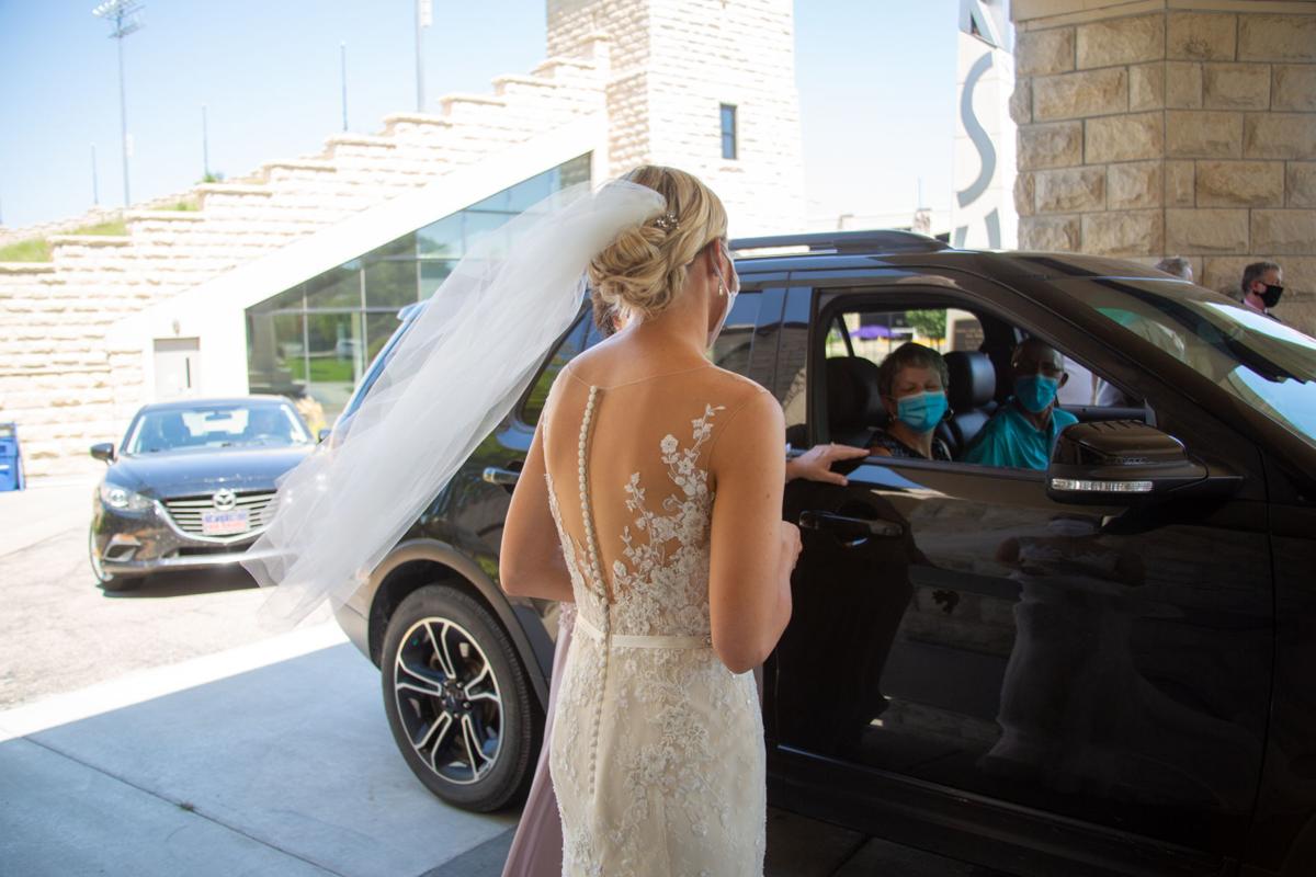 Bride Brittany Murrell greets guests in cars handing them food and gifts. Brittany Murrell and Matthew Lorson held reception at the Alumni center hosting a “drive by wedding” where guests could say their congratulations in the safety of their cars.