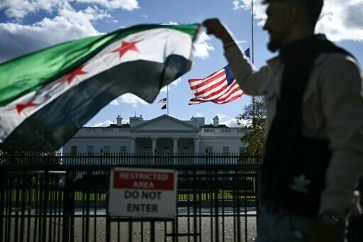 A man holds a Syrian flag across the street from the White House after Syrian President Ahmed al-Sharaa's meeting with US President Donald Trump