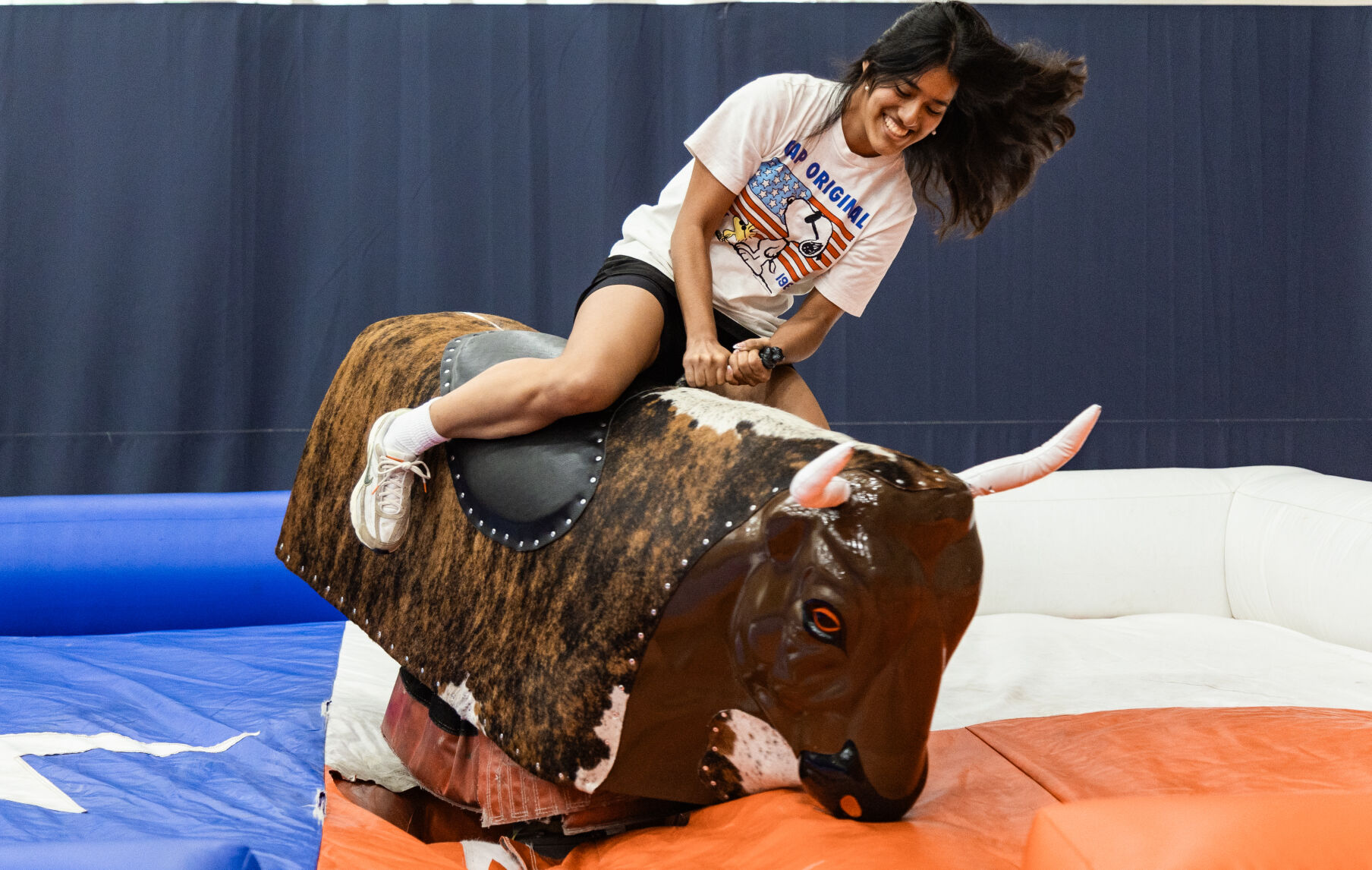 A female student rides a mechanical bull on top of a Texas flag inflatable.
