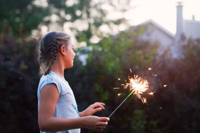 Girl holding sparkler in garden at dusk