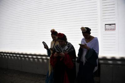 Women in traditional "flamenco" dresses hold their mobile phones outside the Real Maestranza bullring in Seville on April 14, 2024 during de 'Feria de Sevilla' festival. (Photo by CRISTINA QUICLER / AFP) (Photo by CRISTINA QUICLER/AFP via Getty Images)