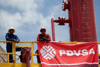 FILE PHOTO: Workers stand in front of a drilling rig at an oil well operated by Venezuela's state oil company PDVSA in Morichal