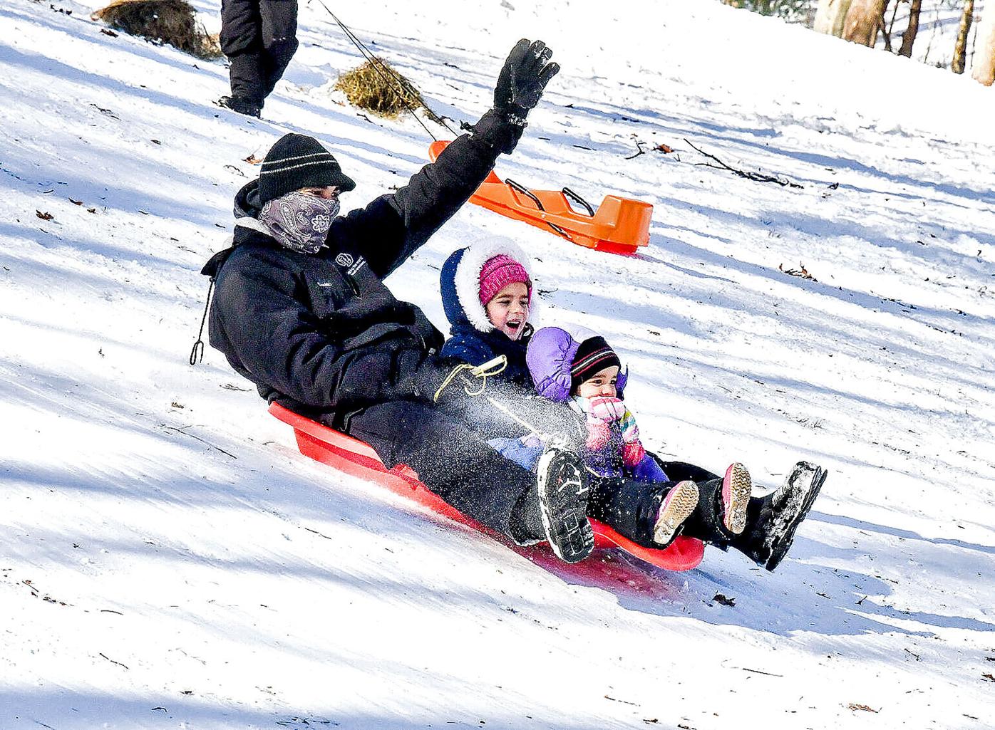 Dad and daughters sledding down the hill