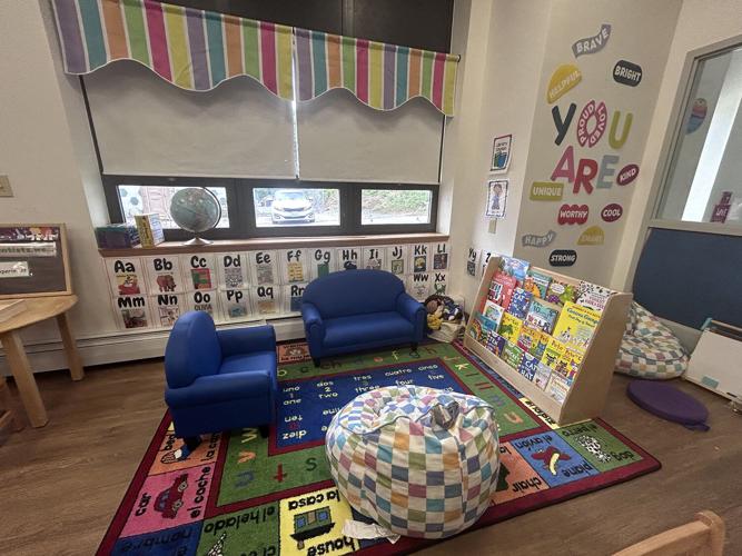 A colorful classroom reading corner with alphabet charts, blue chairs, and a bookshelf filled with children's books.