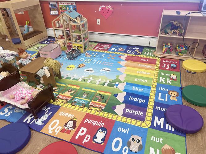A colorful alphabet rug with images of animals and objects is spread on the floor of a playroom.