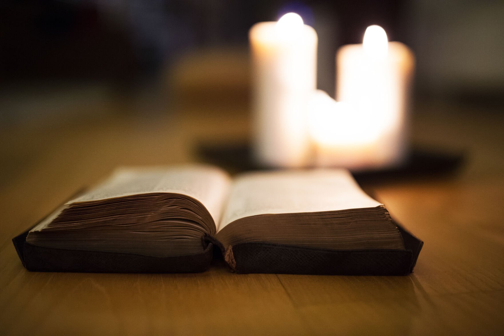 Bible laid on wooden floor, burning candles in the background