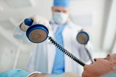 Doctor performing a defibrillator on patient in emergency room