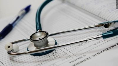 A green stethoscope rests on a doctor's notebook with a blue pen. 
