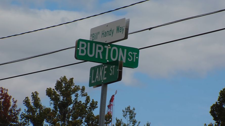 The street signs at the corner of Burton Street and Lake Street. On top is the new sign dedicated to Bill Handy. It reads "Bill Handy Way".