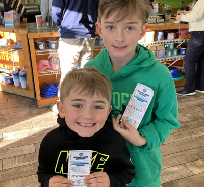 Two children holding up their free bagel certificates from Surf Bagel, earned after completing their reading goals. 