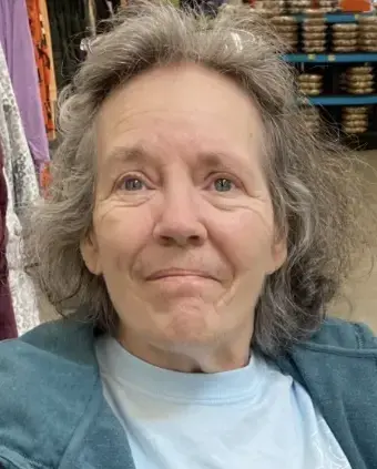 Woman with salt & pepper hair wearing a teal green jacket and blue shirt