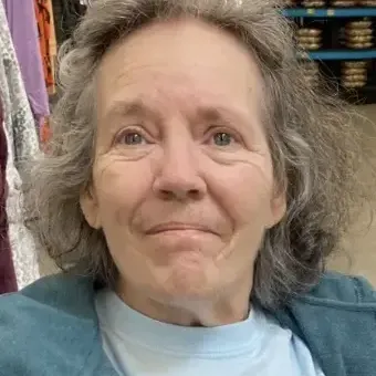Woman with salt & pepper hair wearing a teal green jacket and blue shirt