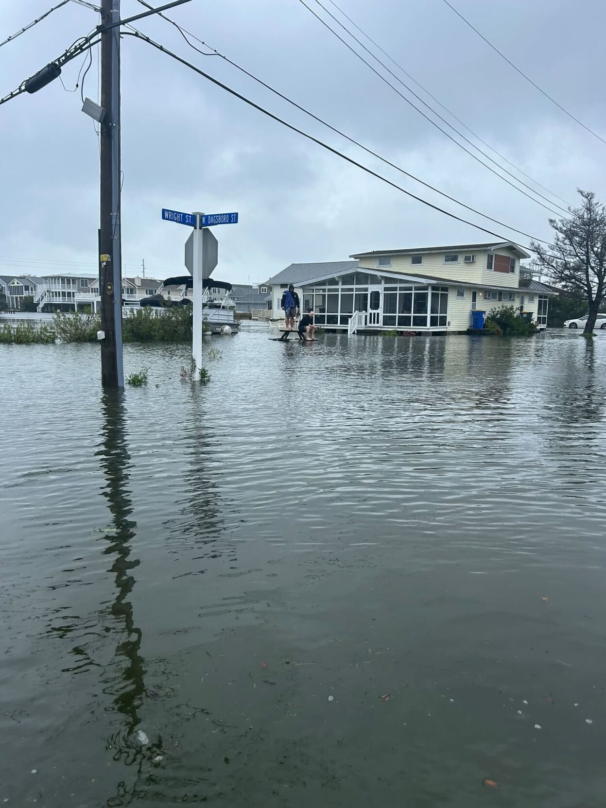 Flooding at W. Dagsboro St. and Wright St. on Fenwick Island, two people perched on top of a picnic table that is half-submerged in the high floodwaters.