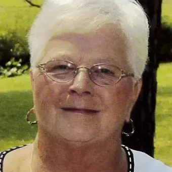 Women with white hair, wearing glasses, and a white sweater in front of a tree 