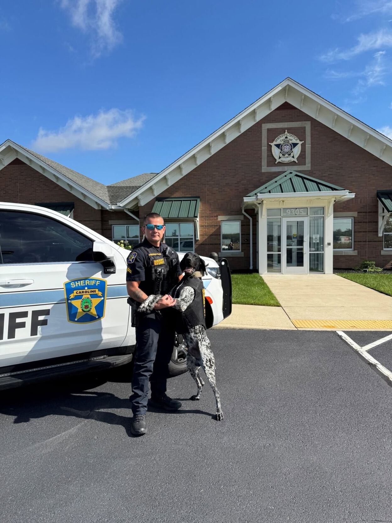 A sheriff's deputy stands next to a k9 wearing a vest.