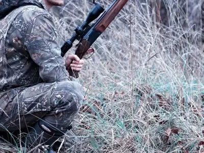 A hunter kneeling in the grass with a gun