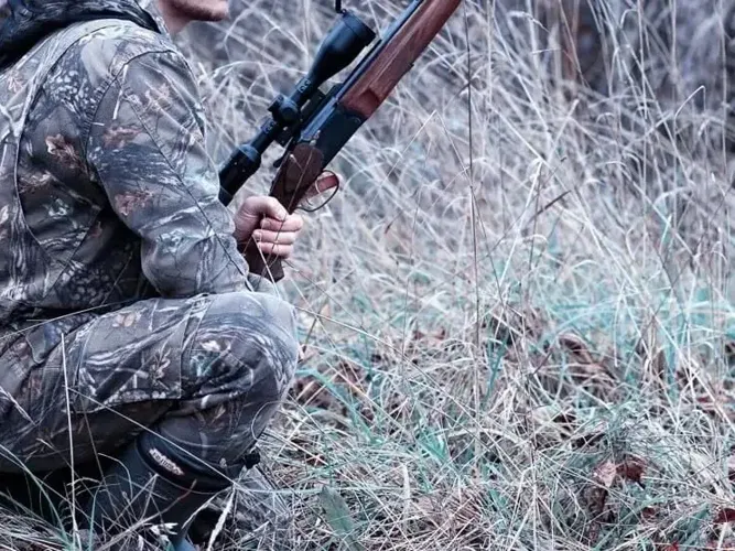 A hunter kneeling in the grass with a gun
