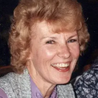 Woman with Red hair, wearing a purple top and gray vest, dark background