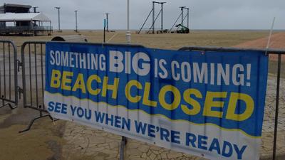 Sign on gate of beach reading "Something BIG is coming! BEACH CLOSED. See you when we're ready."