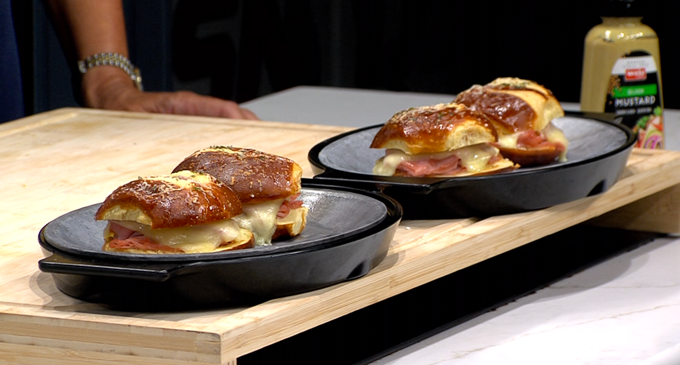 hot ham and cheese sliders, plated on blue plates, sitting on a cutting board with mustard in background