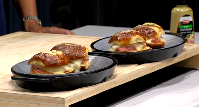 hot ham and cheese sliders, plated on blue plates, sitting on a cutting board with mustard in background