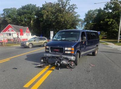Blue van in the middle of the street, with the front on top of a motorcycle.