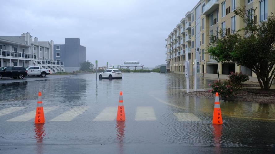 Orange traffic cones block a parking lot that is full of water. One lone white car is parked in the water.