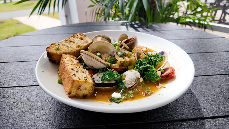 Clams plated on a with White plate with spinach and toasted bread sitting on a black composite round table.