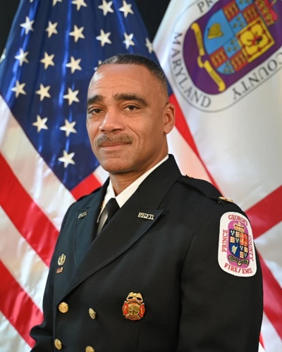 Newly-appointed Maryland State Fire Marshal Chief Caroll Briggs III is pictured in front of an American flag and a Prince George's County flag, wearing a Prince George's County Fire and Emergency Medical Services Department uniform.