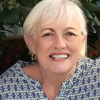 Woman with white short hair small hoop earrings, wearing a blue and white top. 