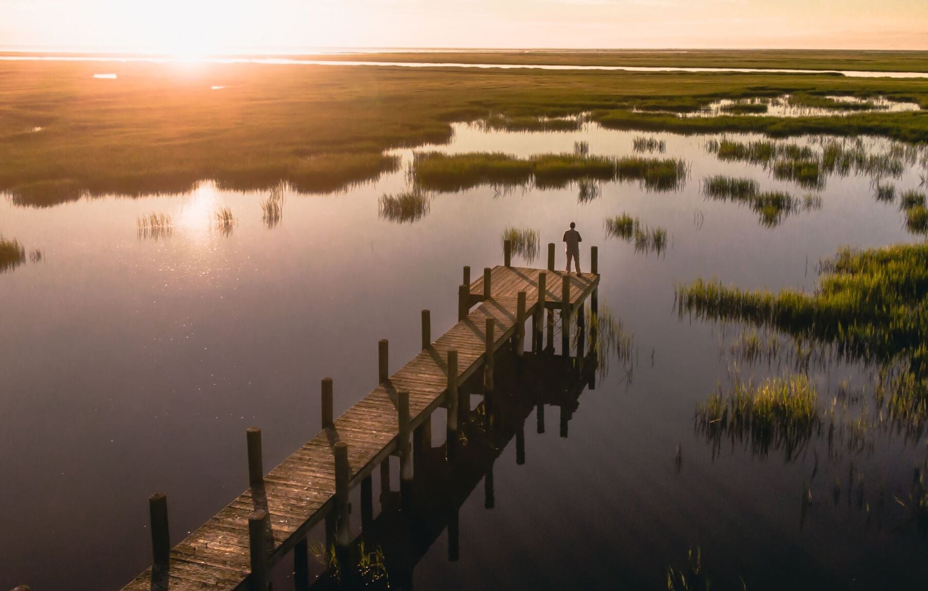 A man fishes from a pier at sunset in an Accomack County marsh
