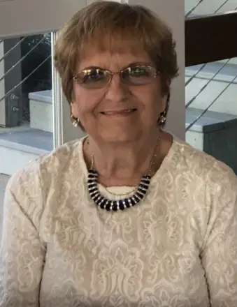 woman with light brown hair wearing a cream color top, glasses, and necklace. 