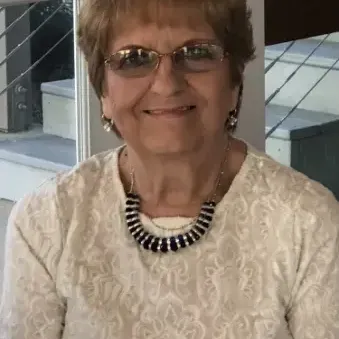 woman with light brown hair wearing a cream color top, glasses, and necklace. 