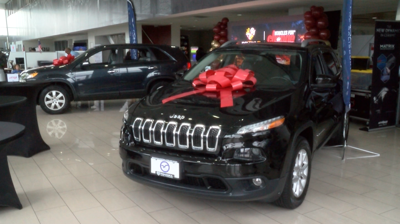 A black SUV on a car dealership showroom floor with a ribbon on the hood.