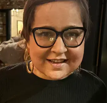 Young lady with black framed glasses, hoop earrings, black mock top.