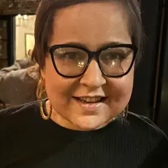 Young lady with black framed glasses, hoop earrings, black mock top.