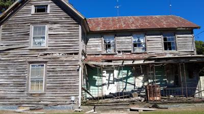 House with broken windows, a roof caving in and damaged siding 