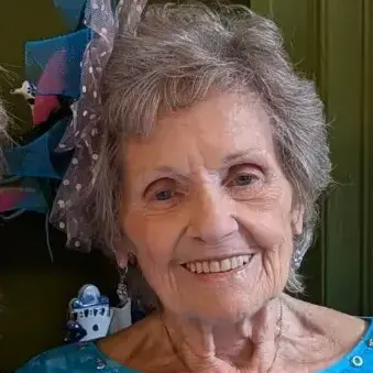Woman with Salt and pepper hair wearing a blue dress and necklace