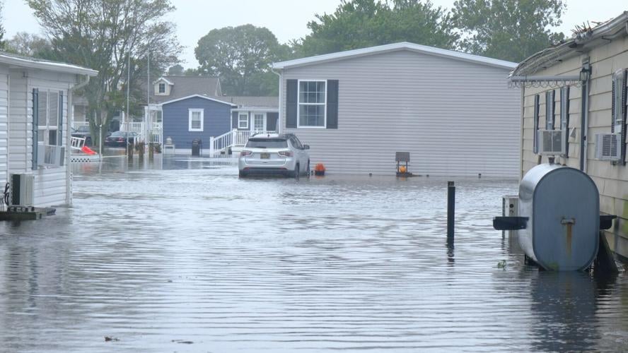 A car parked against a manufactured home. Both are surrounded by water.