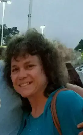 Woman with dark brown hair sprinkled with salt, wearing a blue top and purse strap on her shoulder