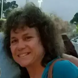 Woman with dark brown hair sprinkled with salt, wearing a blue top and purse strap on her shoulder