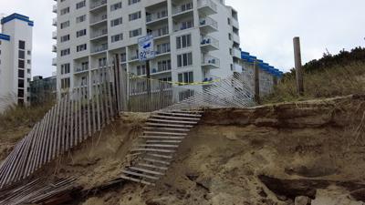 A wall of sand a few feet high with a wooden fence draped over it from storm damage. 92nd street sign along the walkway. 
