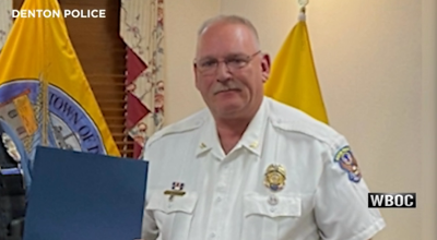 Late Denton Police Chief George Bacorn holds up a blue envelope as he faces the camera.