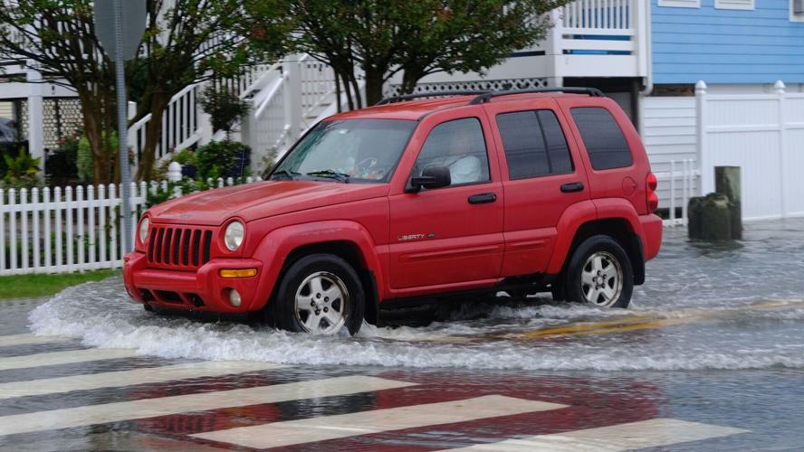 A red Jeep pushes water on a flooded street as it approaches a crosswalk.
